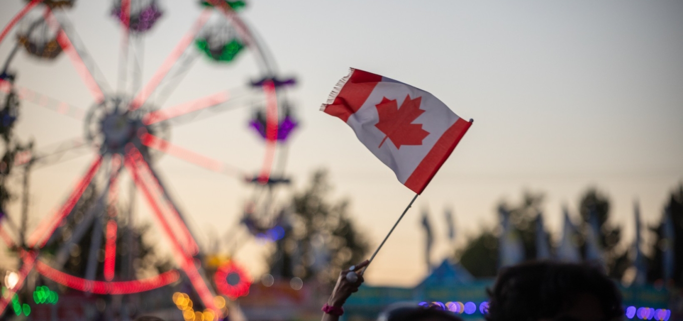 A person waving a Canadian glad in front of a ferris wheel.